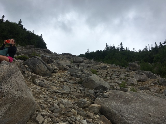 Hiker drinking water on rock slide trail.