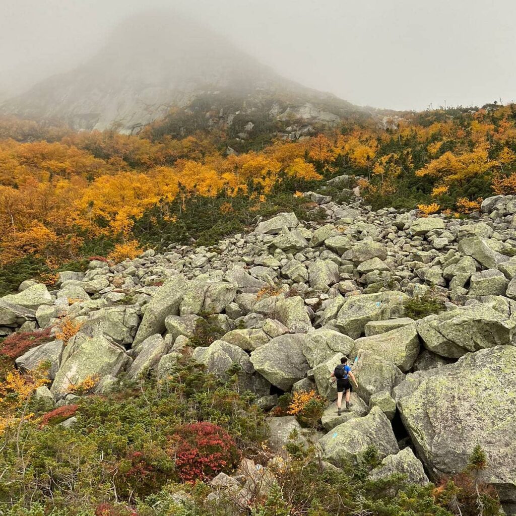 Hiker entering boulder field with mountain peak in the fog.