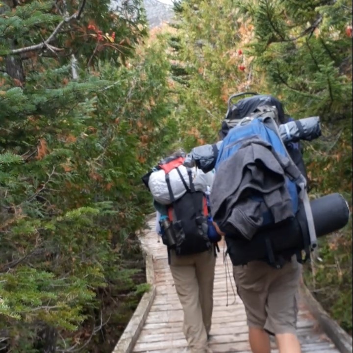 Two backpackers hiking on wooden bridge.