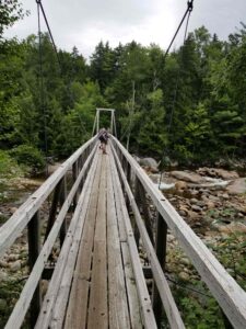 Hikers crossing narrow wooden bridge.
