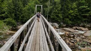 Hikers crossing narrow wooden bridge.