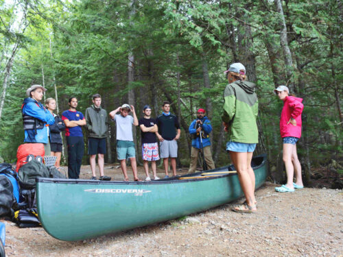 Group standing around a canoe listening to instructor