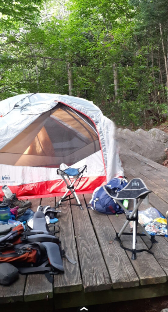 Campsite setup with tent and chairs on a wooden platform.
