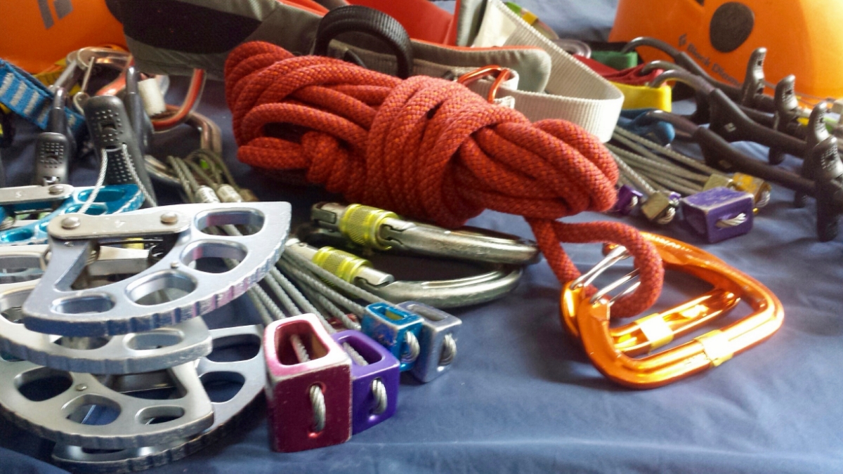 Image of climbing gear: (from left to right) a Cam, some nuts, carabiners, accessory cord, a harness, more nuts, more cams and a helmet.