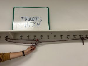 Rope hanging off of hangers below a sign that says 'trucker's hitch'