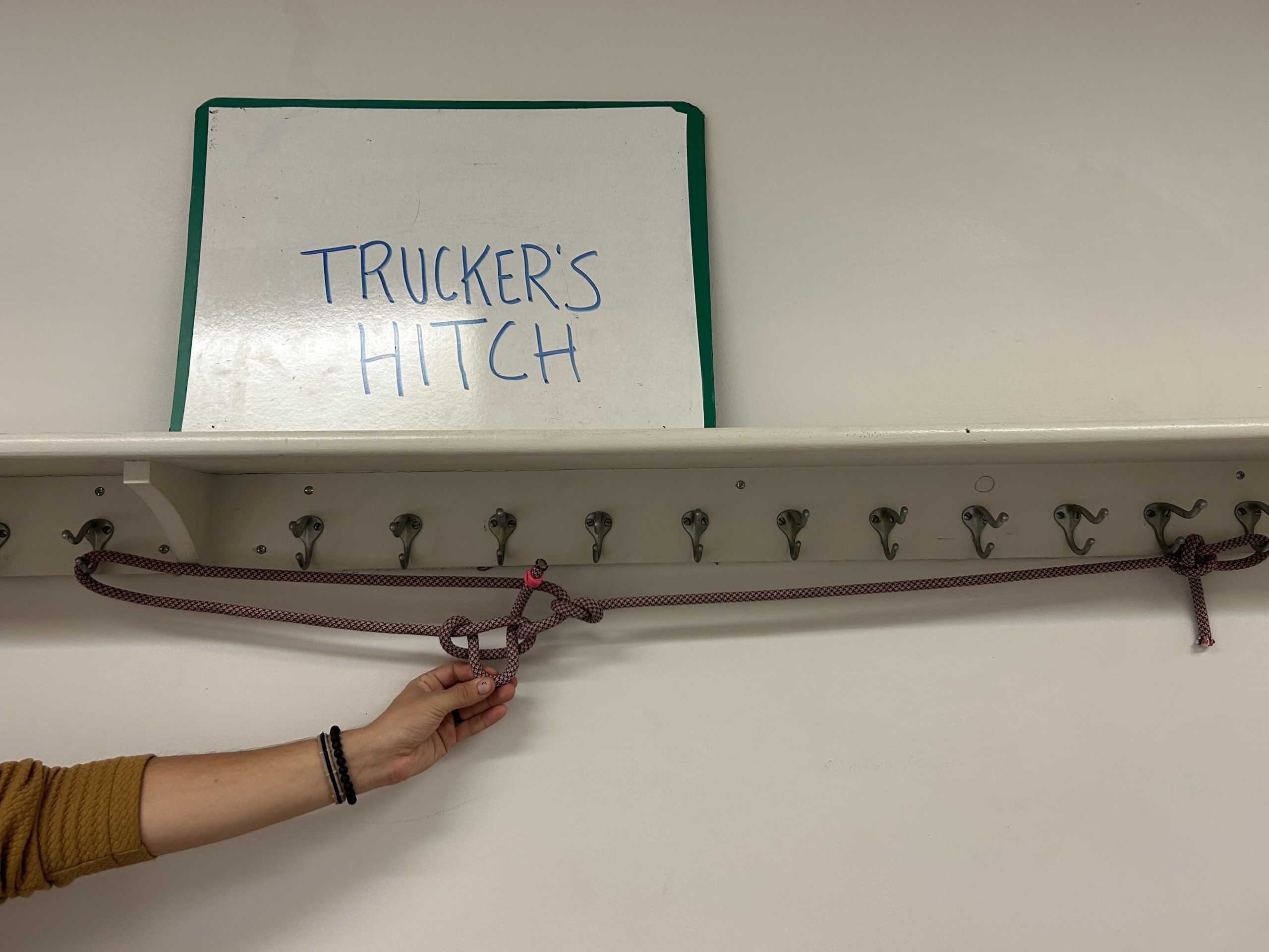 Rope hanging off of hangers below a sign that says 'trucker's hitch'