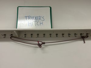 Rope hanging off of hangers below a sign that says 'trucker's hitch'