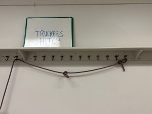 Rope hanging off of hangers below a sign that says 'trucker's hitch'