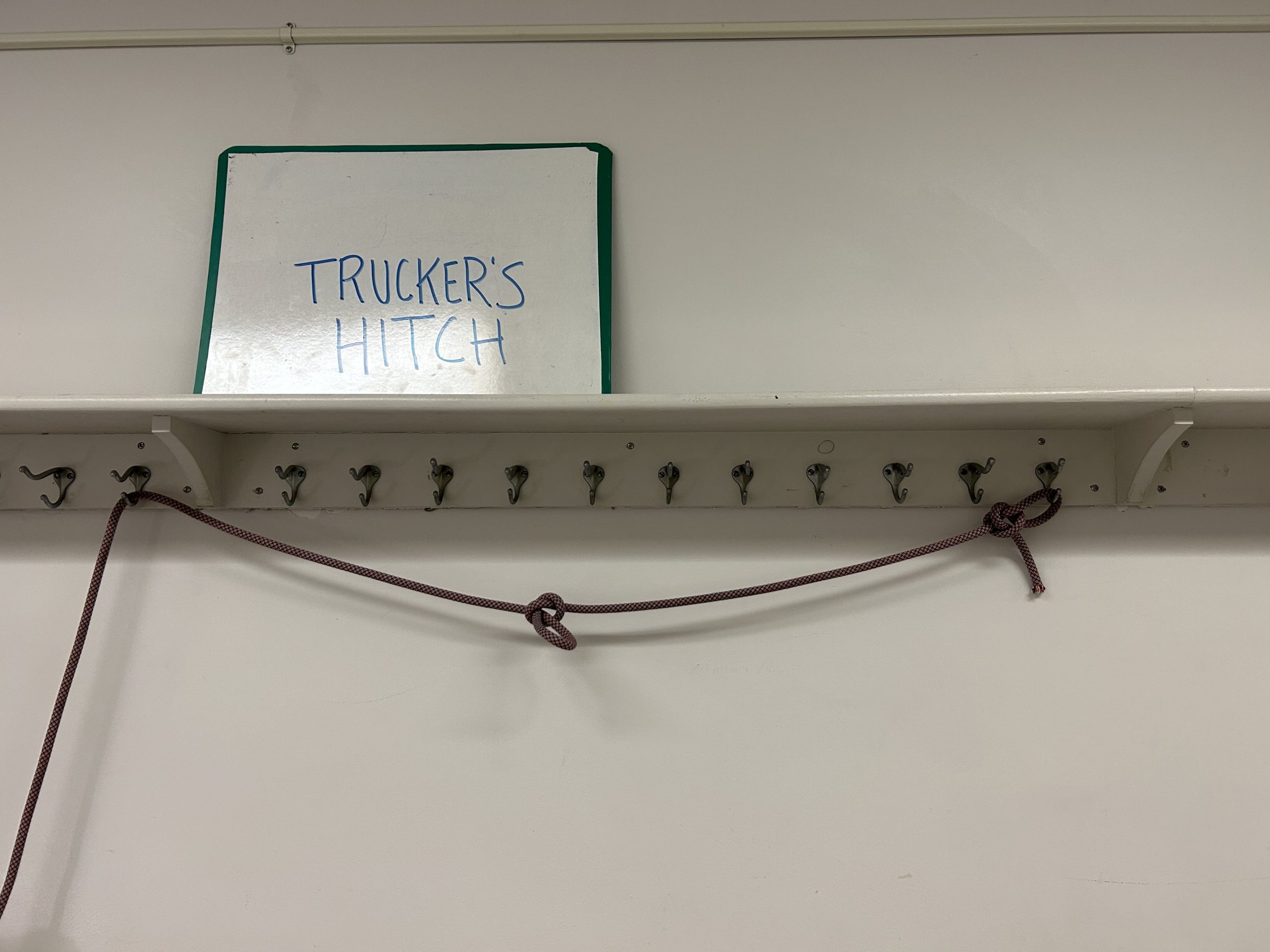 Rope hanging off of hangers below a sign that says 'trucker's hitch'