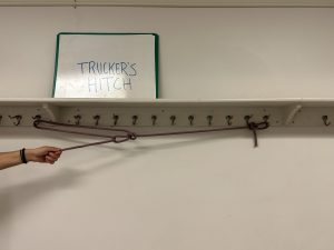 Rope hanging off of hangers below a sign that says 'trucker's hitch'