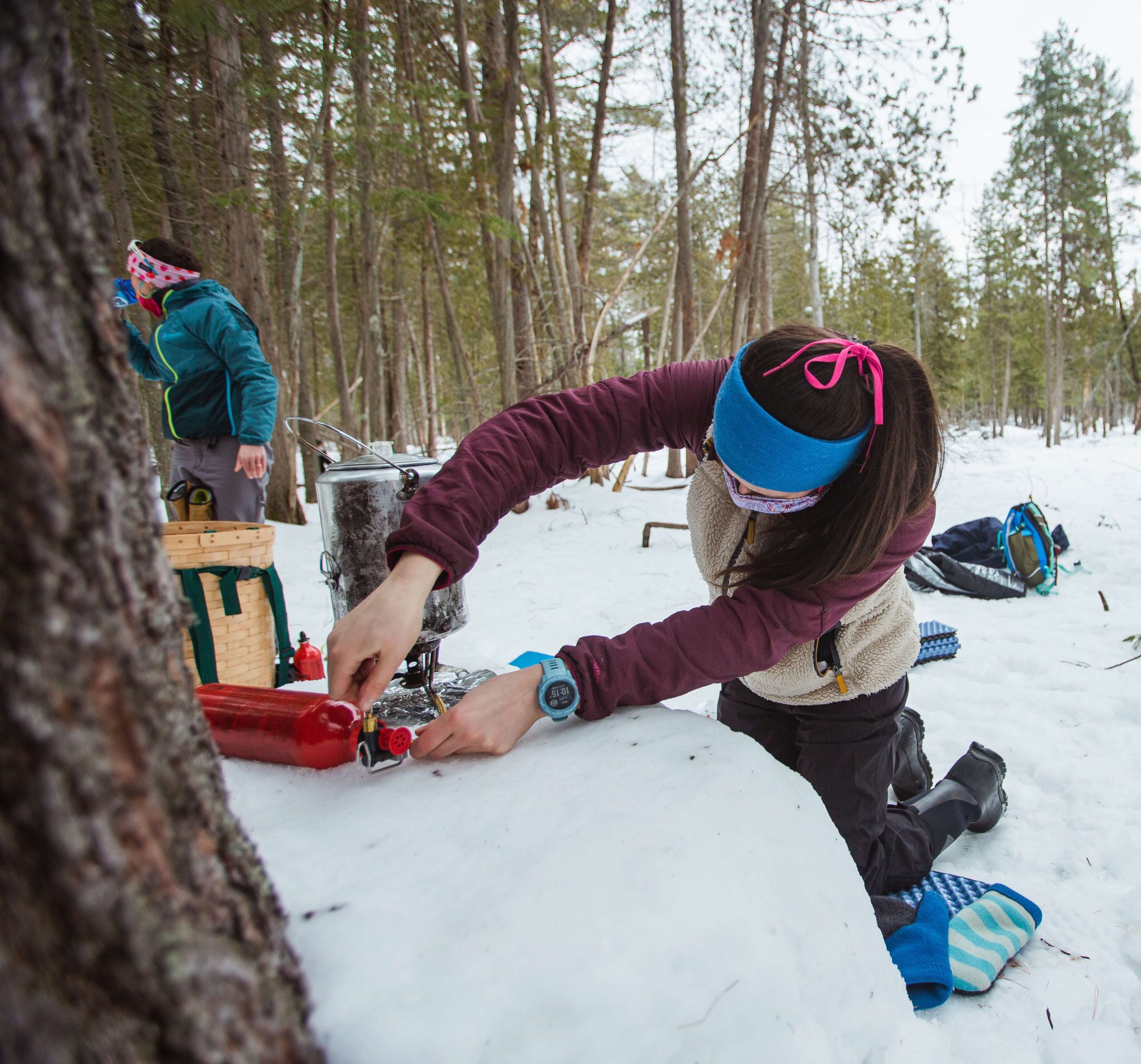 A camper is adding pressure to a msr white gas fuel bottle while setting up a stove in a winter campsite.