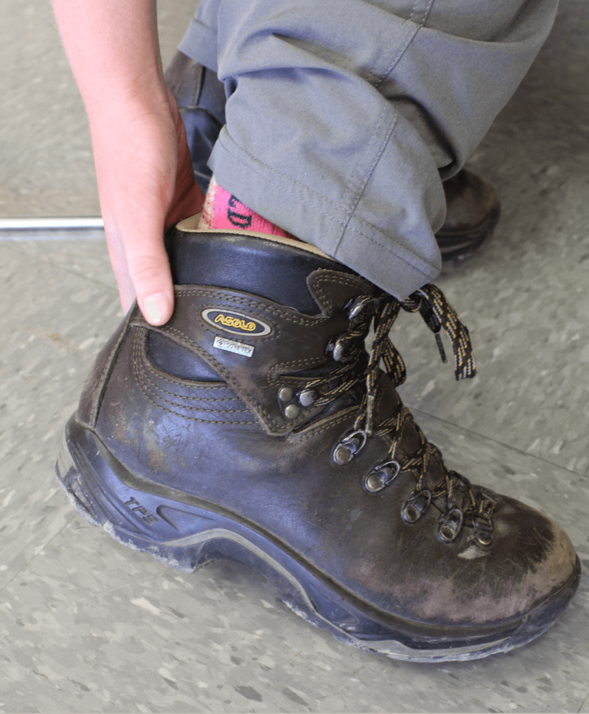 Student rubbing a blister on their heel in hiking boots.