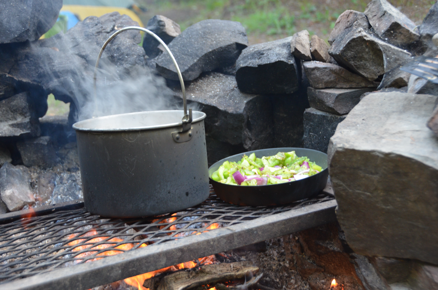 A pot an a pan are being cooked over a campfire