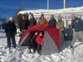Photo of nine UMaine students in the snow with a tent