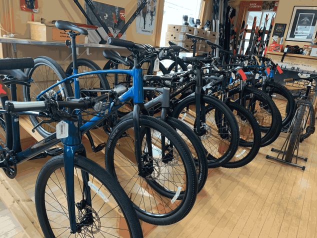 A row of mountain bikes with price-tags on them inside a bike shop.