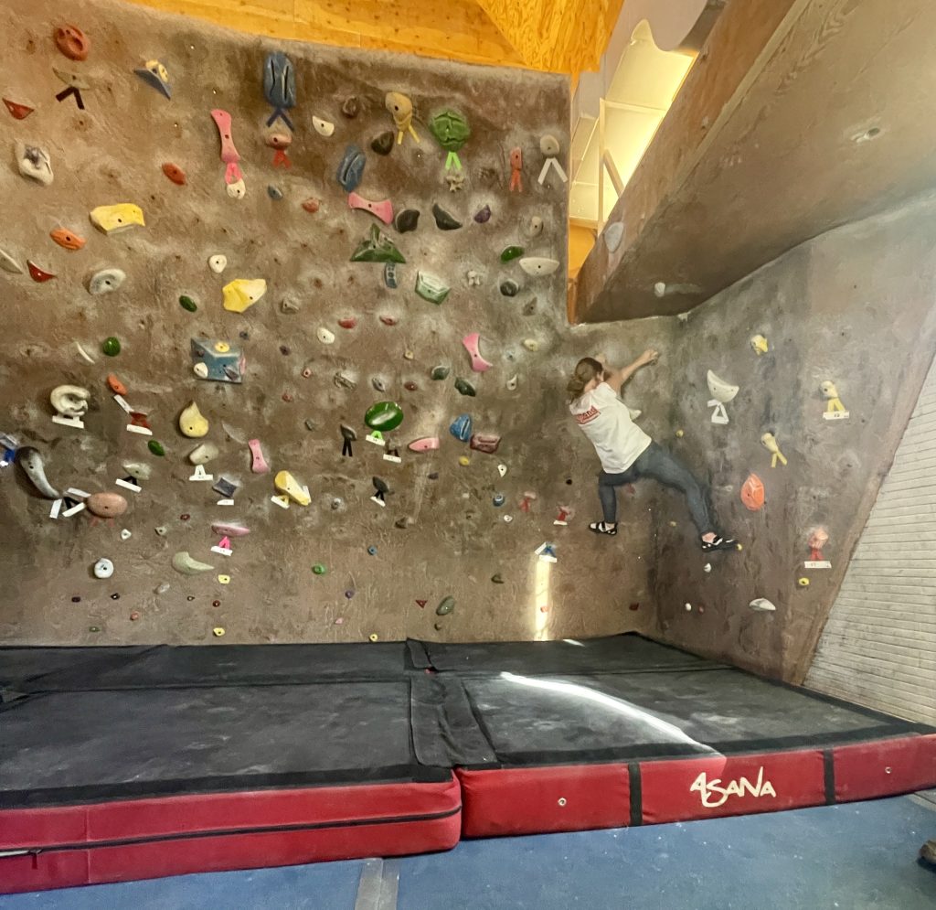 A climber bouldering on the boulder wall at a rock climbing gym.