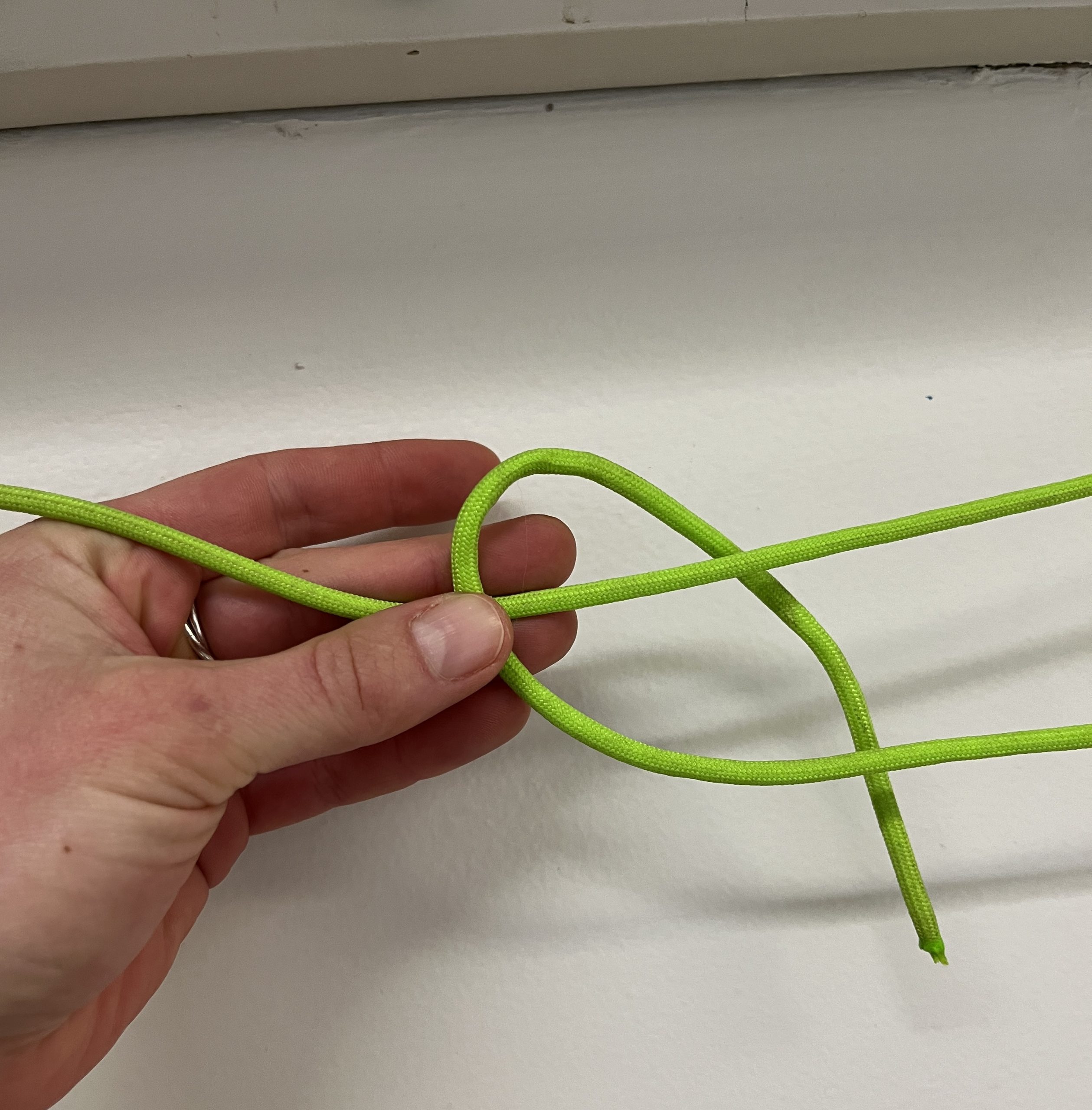 Loop of green cord being held by hand in front of white wall.