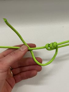 Working end of green cord in a taut line hitch being held by hand in front of white wall.