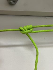 Completed taut line hitch close-up with green cord in front of white wall.