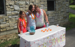 three girls, outside, at a table selling beverages
