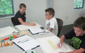 three boys sitting at a table working on classroom lessons