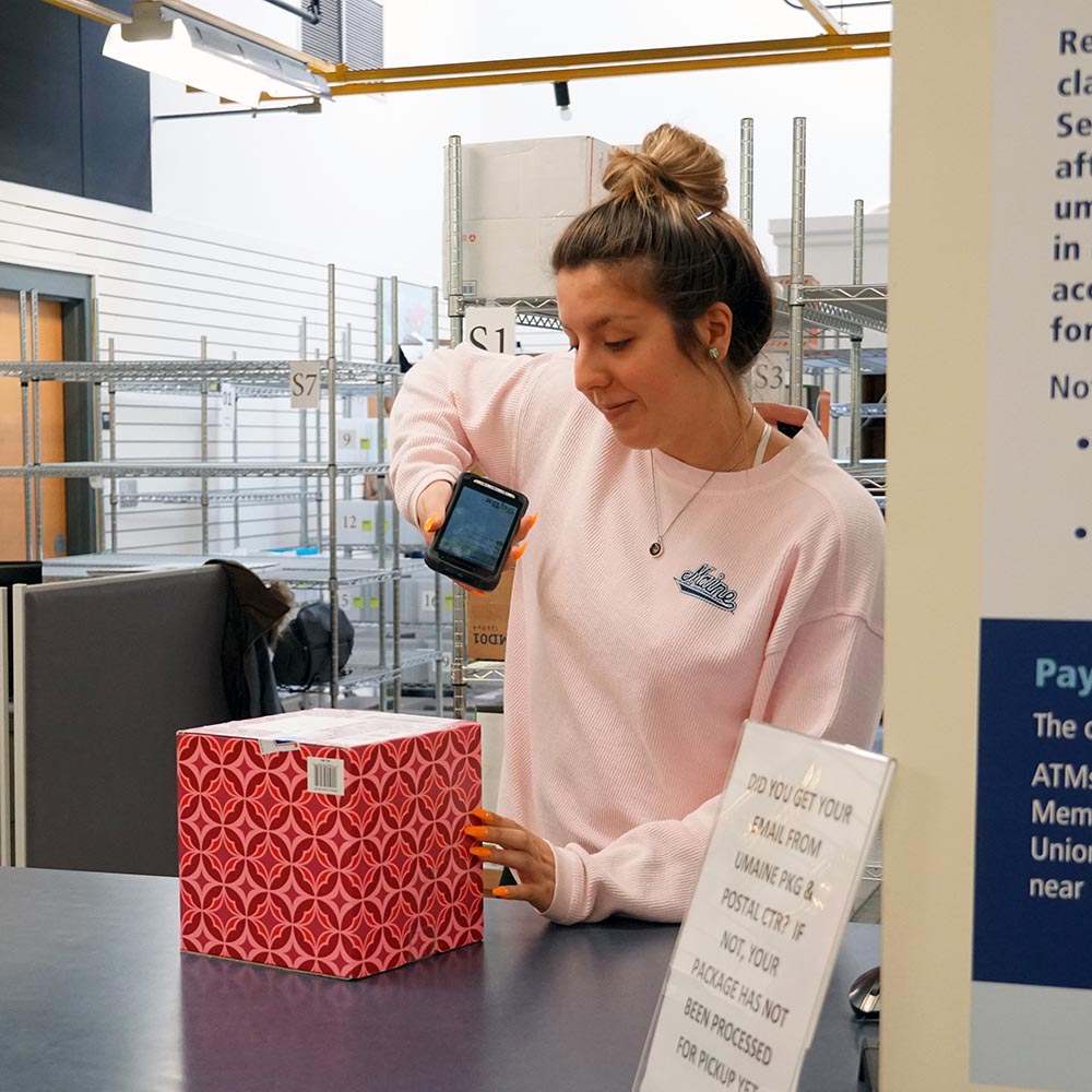 A staff member scans a patterned pink package at a mail center counter.