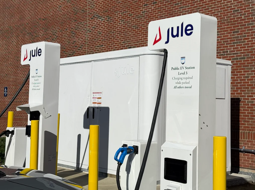 Two white Jule Level 3 public EV charging stations stand in front of a brick building.