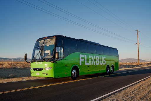A bright green FlixBus traveling on a paved two-lane road through a desert landscape.