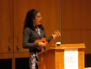 L.E. Leone playing a ukulele and signing behind a podium
