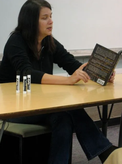 Lydia Millet sitting behind a desk reading aloud a book