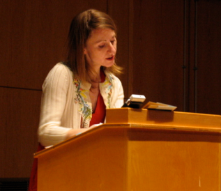 Mel Nichols reading aloud behind a podium