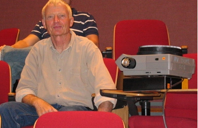 Robert Grenier sitting in an auditorium looking at the camera