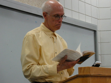 Robert Pagett reading a book while standing behind a podium