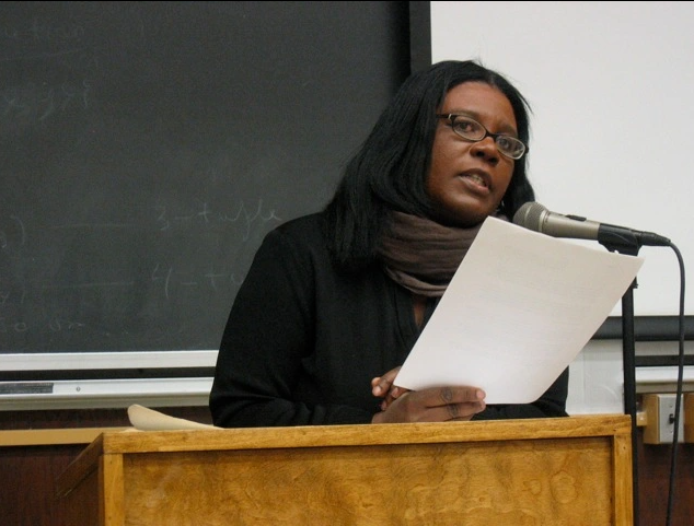 Claudia Rankin reading in front of a blackboard behind a podium