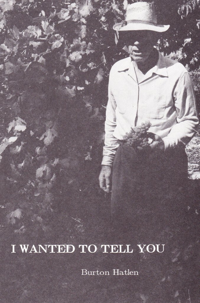black and white photo of a man wearing a hat and a white collared shirt staring blankly at the camera with flowers in one hand