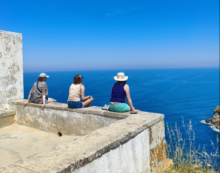 Three people sitting on the edge of a wall looking out at the ocean in Portugal