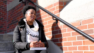 Photo of 2022 UMaine Machias valedictorian Yani Nganzobo sitting on library steps at the Machias campus