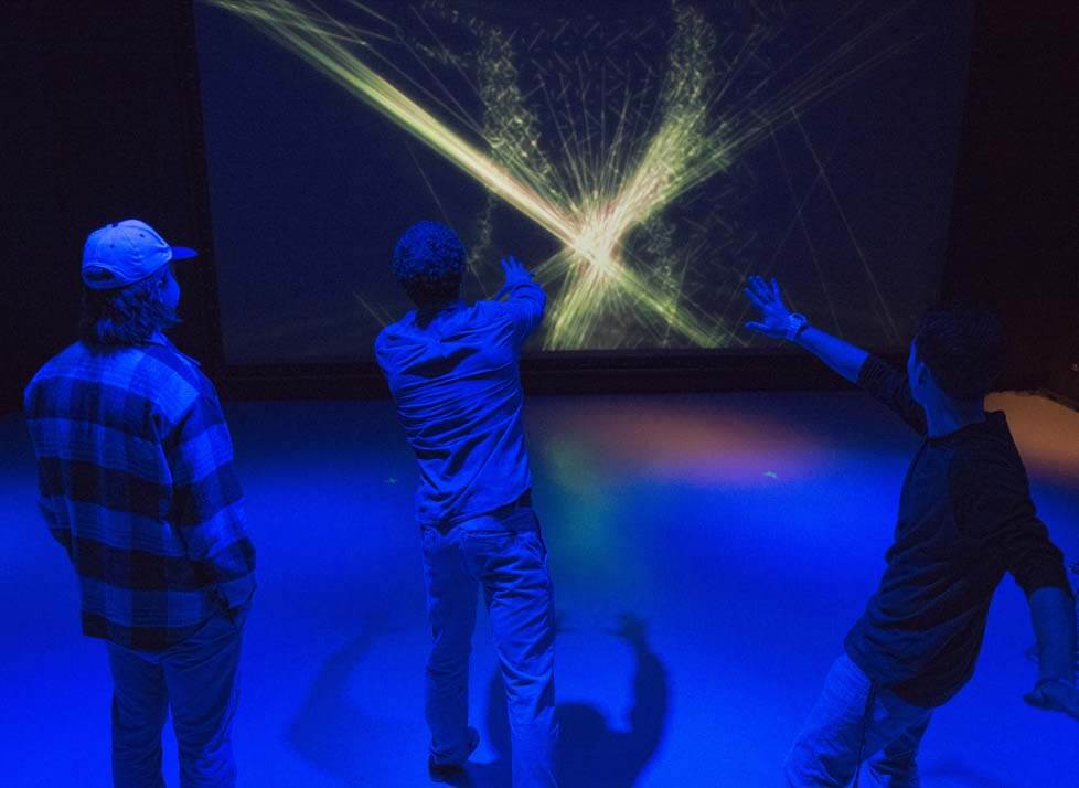 A photo of three people in front of a large screen