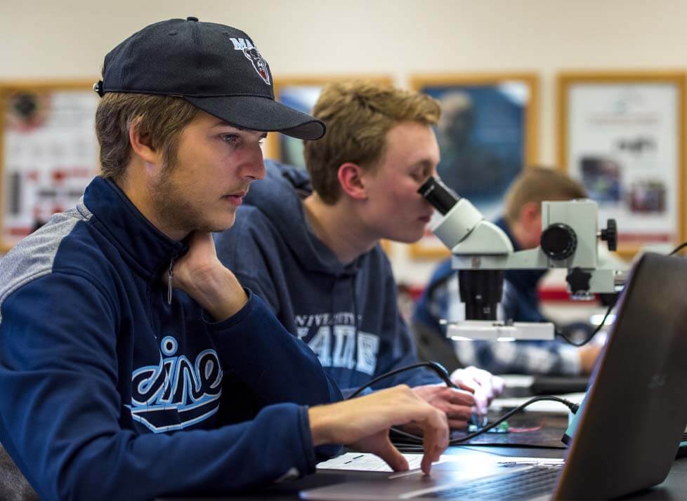 A photo of two people, one is looking through a microscope