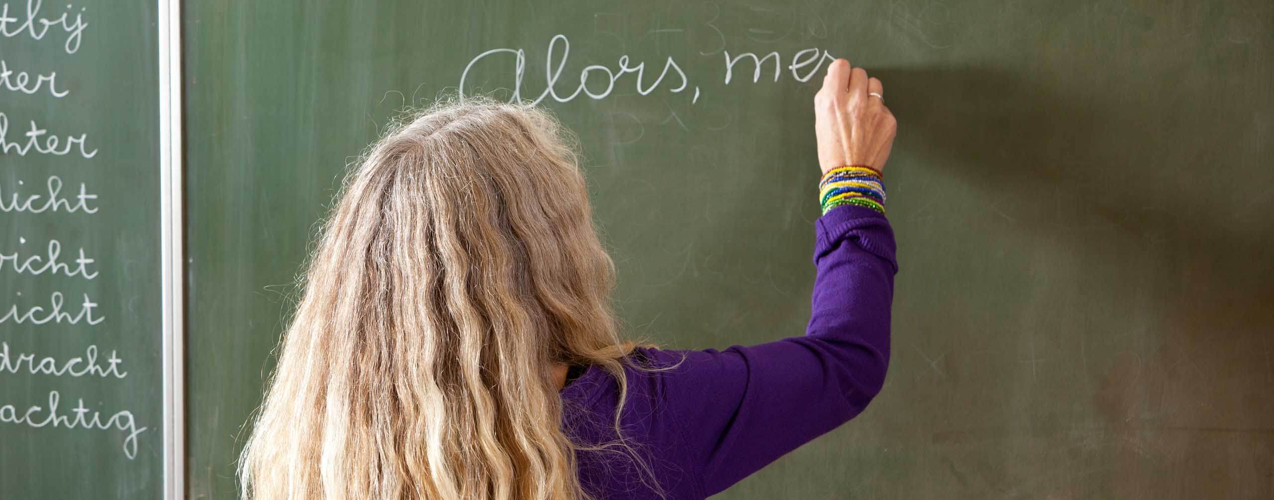 A photo of a person writing on a black board in French
