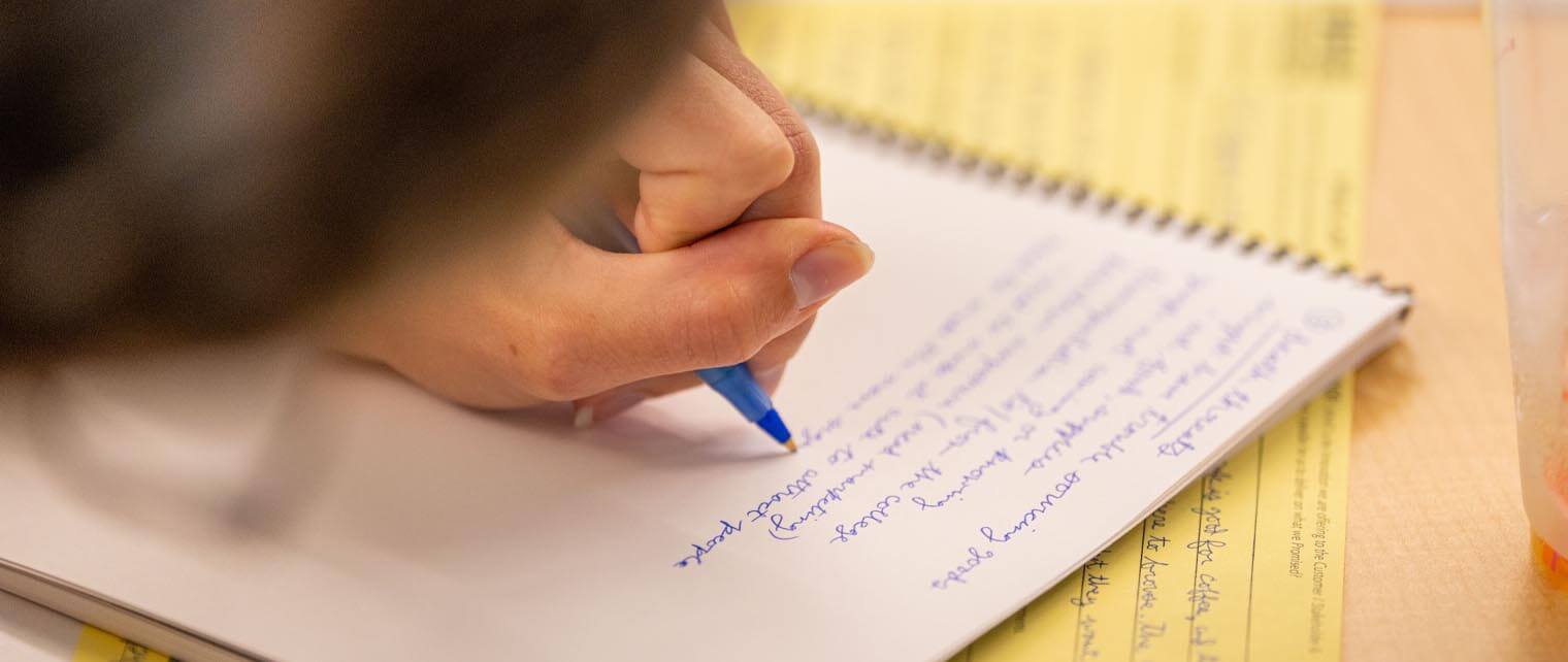 A photo of a hand holding a pen writing in a notebook