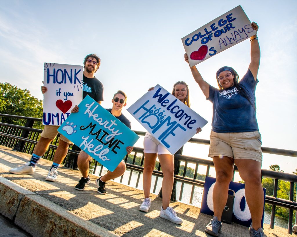 Photo of UMaine students on a bridge holding creative signs showing school spirit.