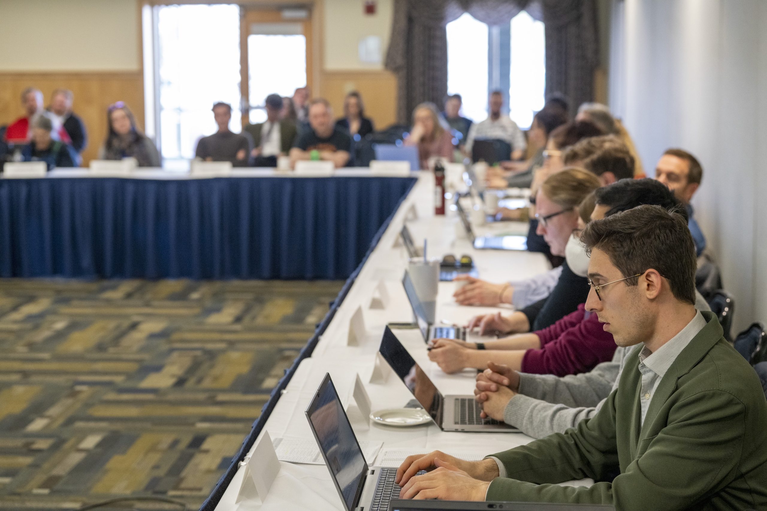 UMaine Faculty Senate in session. Senators sit at a long table, many typing on their laptops.