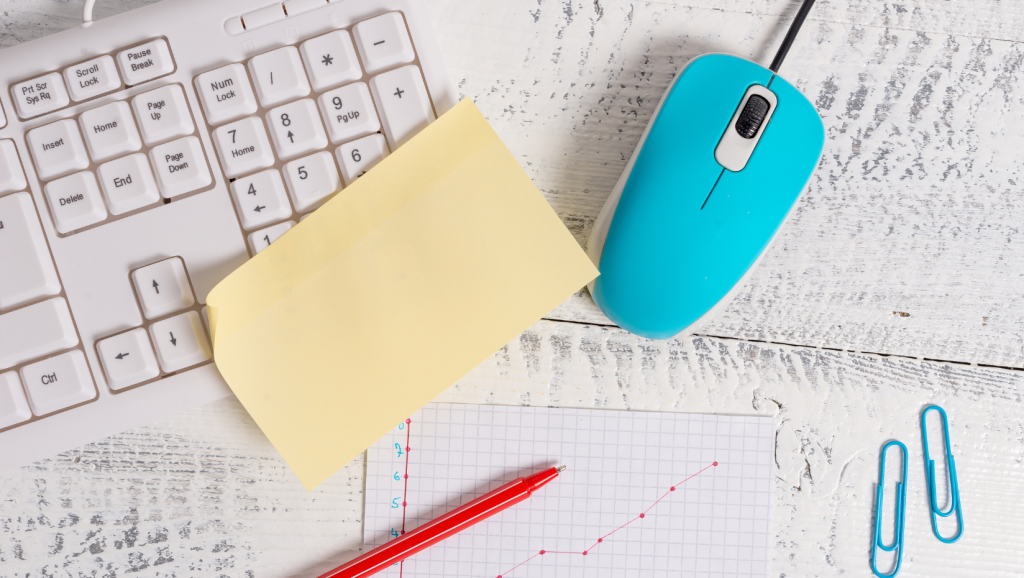 Keyboard with blue mouse, yellow post-it note, red pen, 2 blue paperclips, line graph drawn on graph paper