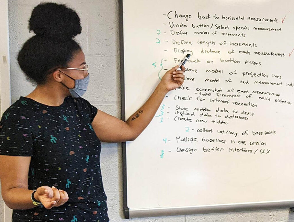 A woman points at a dry erase board