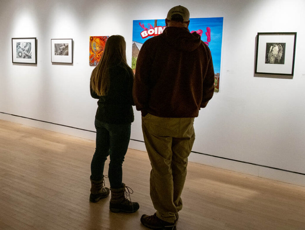 Two people look at artwork on in a gallery