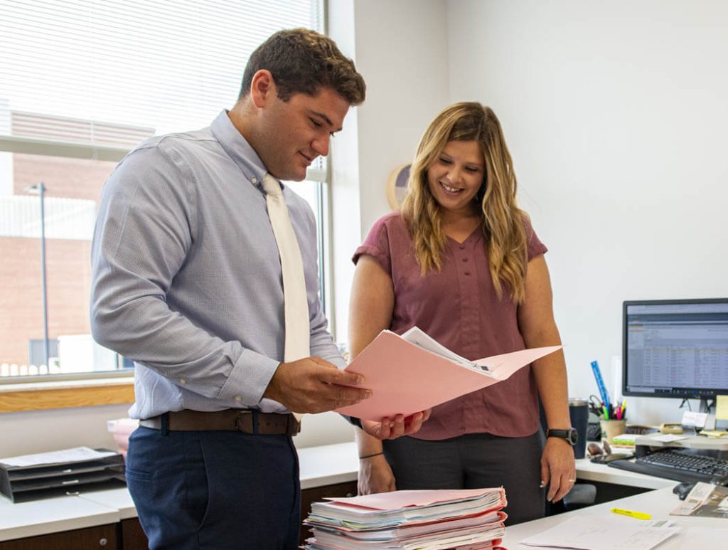 A photo of two people standing in an office looking at papers
