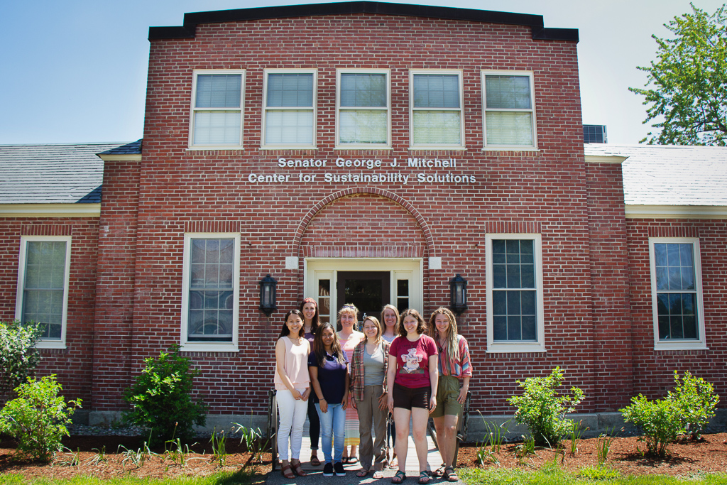 Charlotte Rhodes, MacKenzie Conant, Morelys Rodriguez Alfonso, Brooke MacDonald, Sara McBride, Shayla Miller, Molly Bennett and Jessica Beneski stand in front of Mitchell Center.