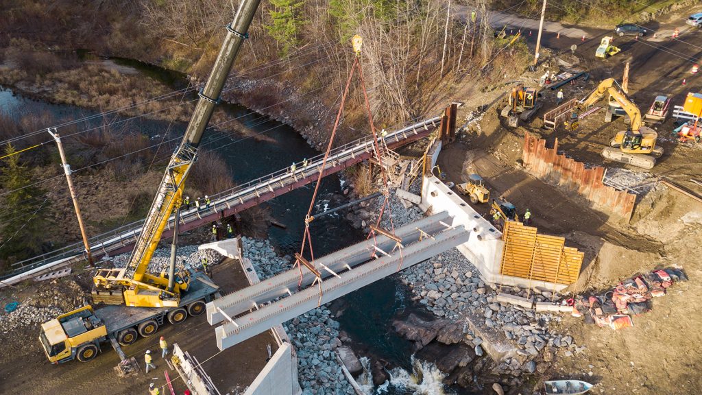 A crane lifts a bridge girder into place over a river.