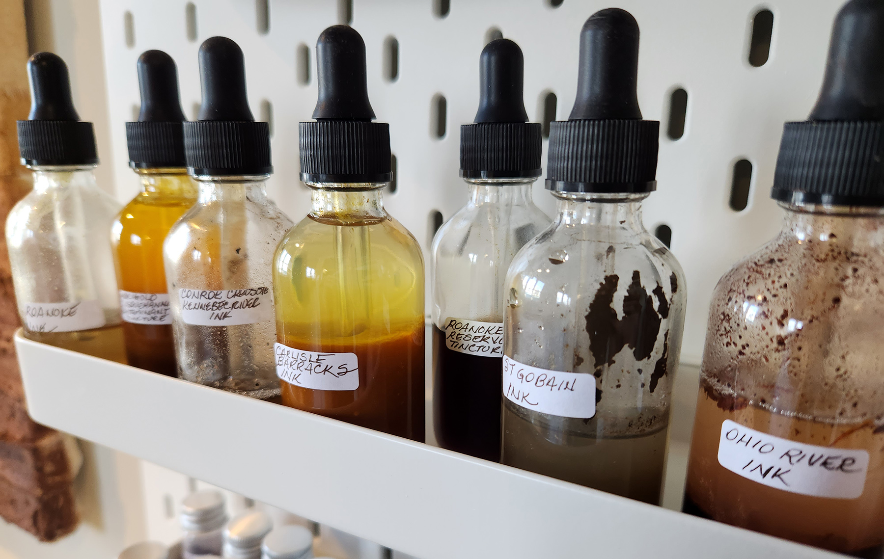 Vials containing PFAS contaminated materials on display in Radical Gardening. Vial labels include "Ohio River ink" and "Roanoke Reservoir Tincture"